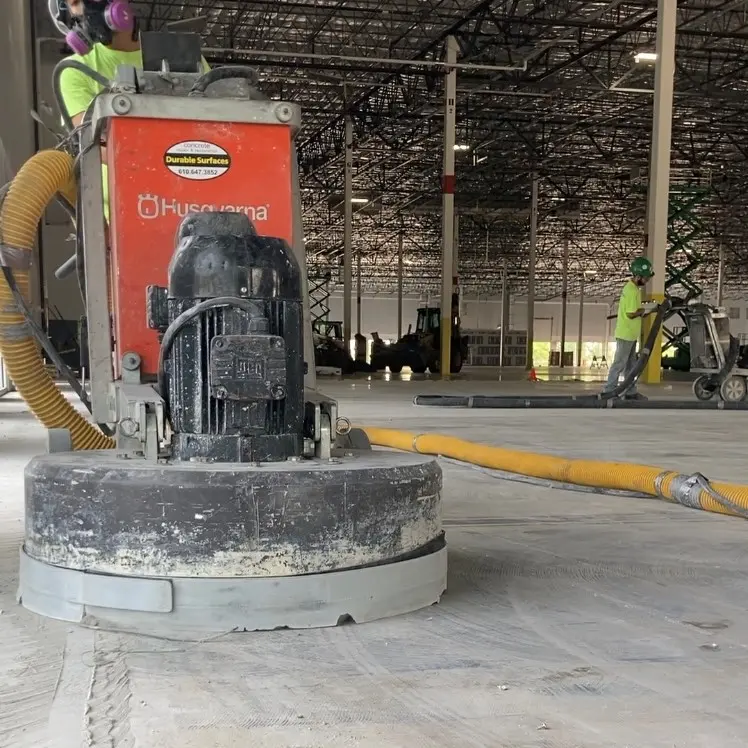 Worker using a concrete floor grinder in a warehouse